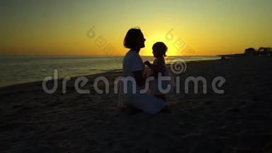 日落时分，年轻漂亮的女人和她的小女儿在海滨散步。 妈妈把女儿抱在怀里。 他们